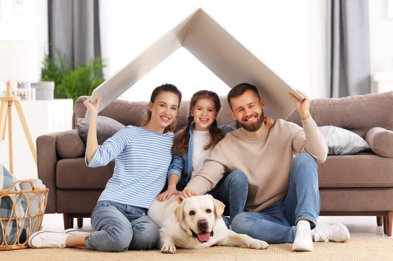 Happy family with their dog sitting under a roof symbolizing home security and rental stability.