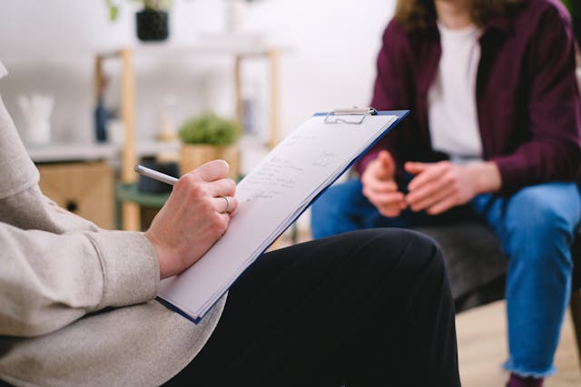 Landlord taking notes on a clipboard during a conversation with another seated individual